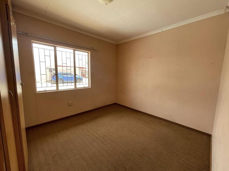 An empty bedroom featuring built-in cupboards, carpeted flooring, and security bars on the window.