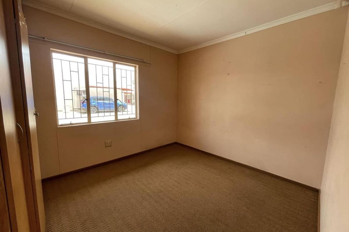 An empty bedroom featuring built-in cupboards, carpeted flooring, and security bars on the window.