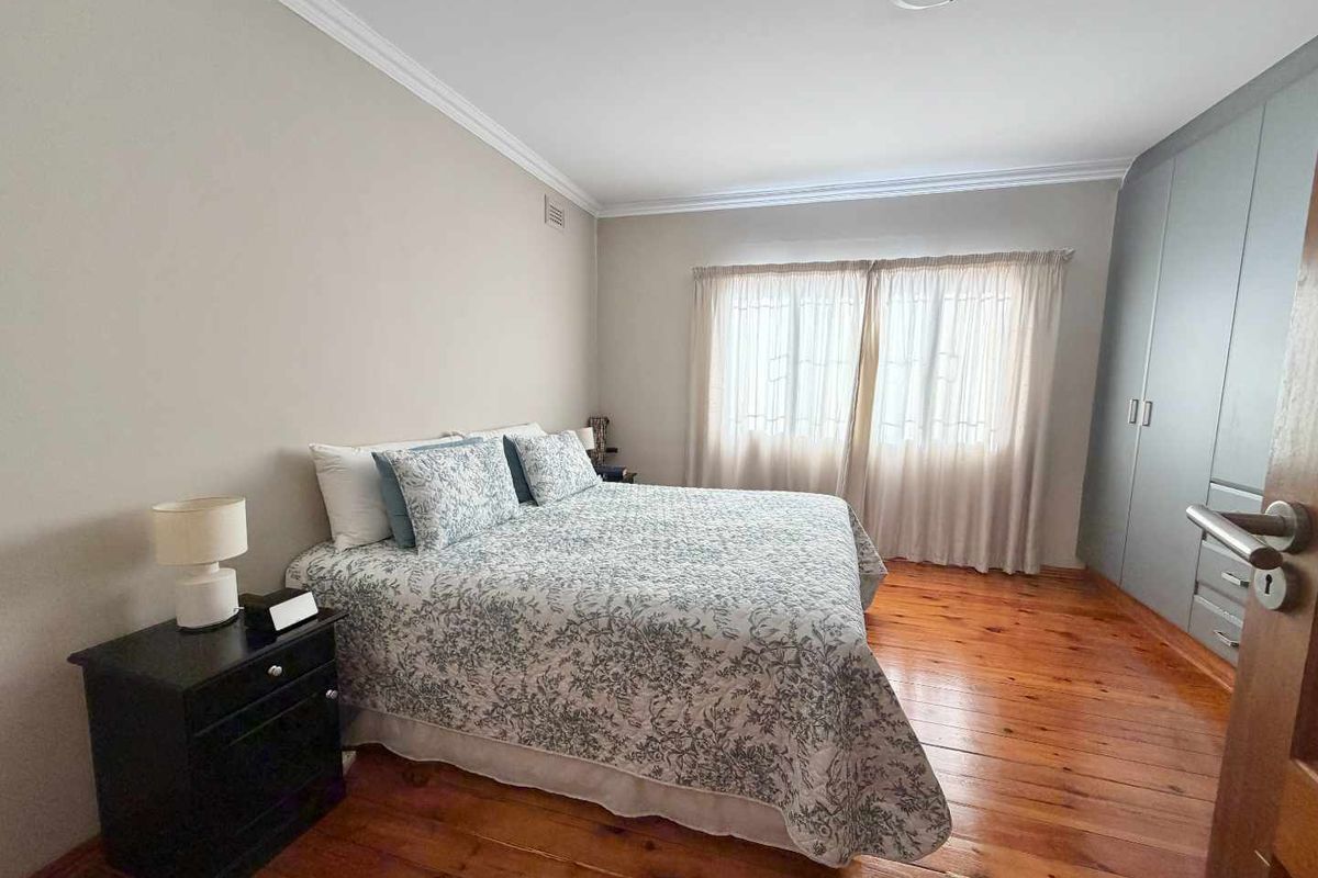 A bedroom featuring polished timber flooring, built-in cabinetry, and neutral wall tones, providing a functional and comfortable living space.