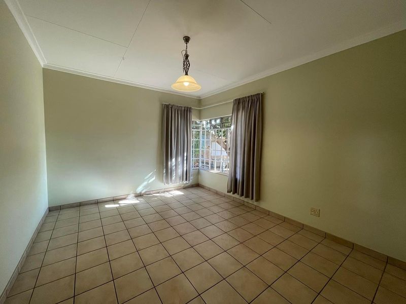 An empty bedroom featuring tiled flooring, a corner window, and a central pendant light fixture, offering a blank canvas for personalization.