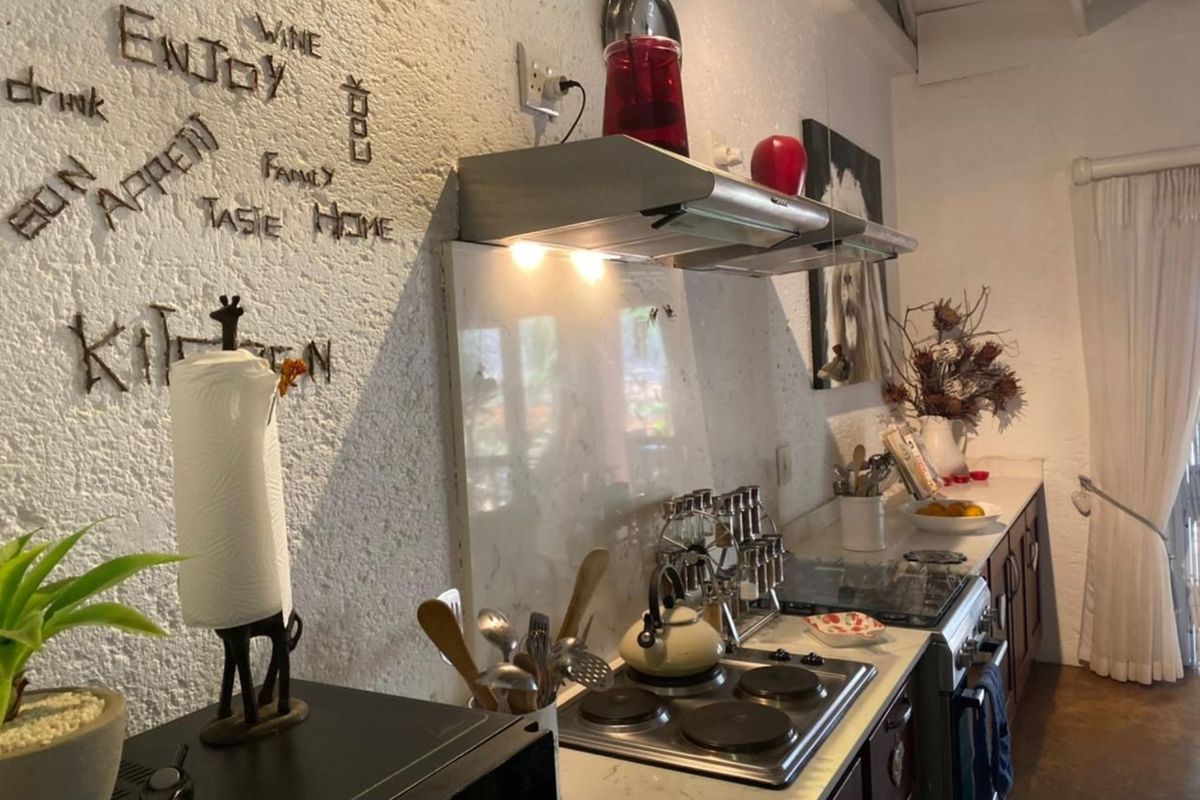 A functional kitchen featuring a built-in electric hob, stainless steel extractor fan, and stone-look countertops against a textured wall finish.
