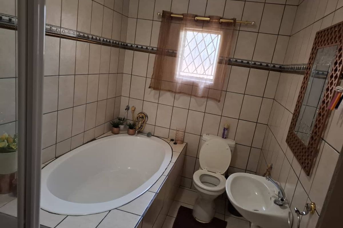 A compact bathroom featuring a built-in bathtub, a standard toilet, and a wall-mounted basin with full-height wall tiling.