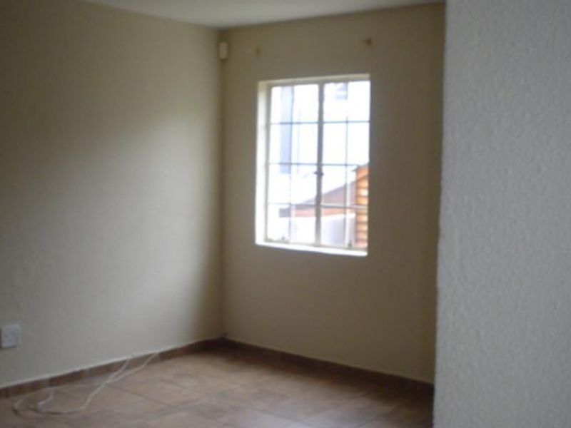 An empty bedroom featuring tiled flooring and a window with security bars, providing a blank canvas for potential interior design.