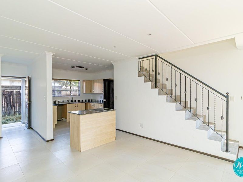 Open plan living area featuring a kitchen with light wood cabinetry, a central island, and a staircase with a decorative wrought iron balustrade.