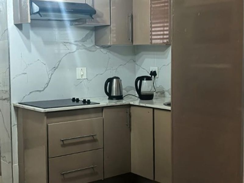 A compact, modern kitchen featuring sleek cabinetry, marble-look splashbacks, an integrated electric hob with extractor fan, and stylish pendant lighting.