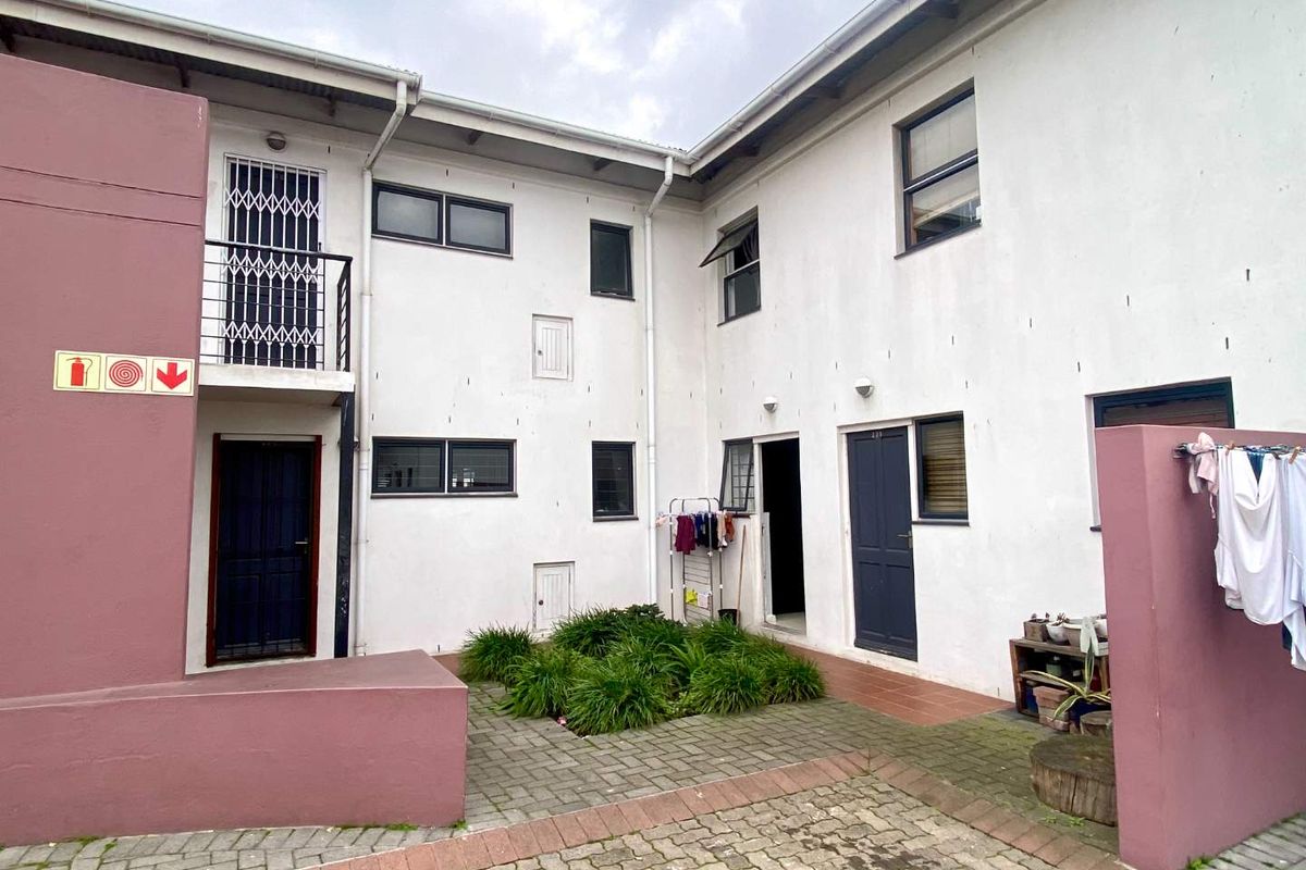 Rear courtyard area of an apartment complex featuring paved surfaces, a small garden bed, and access to multiple residential units.