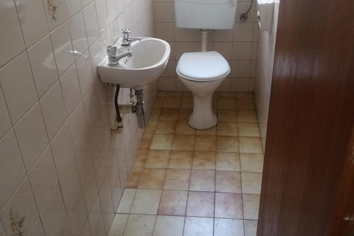 A compact guest bathroom featuring a wall-mounted basin and a standard toilet, finished with dated ceramic wall and floor tiling.