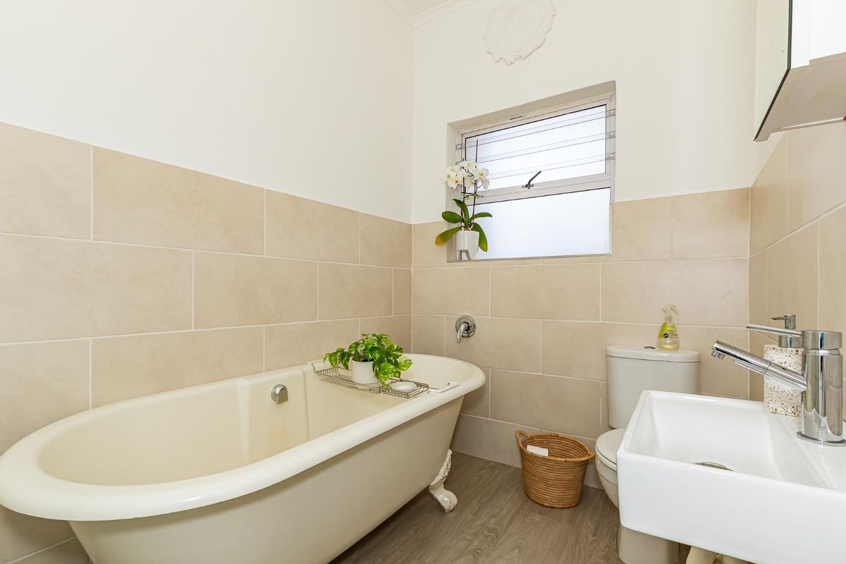 A functional bathroom featuring a classic clawfoot bathtub, a modern wall-mounted basin, and neutral wall tiling.