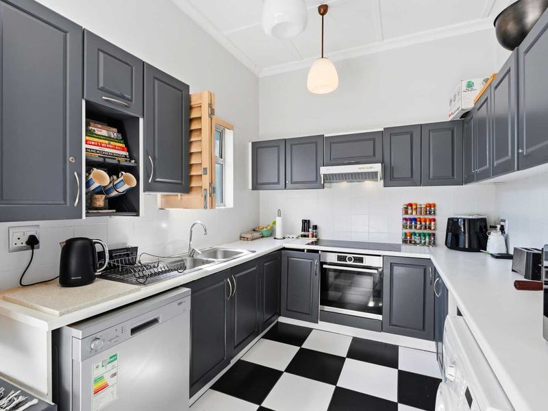 A well-maintained kitchen featuring dark grey cabinetry, white countertops, a built-in oven with hob, and classic checkerboard floor tiling.