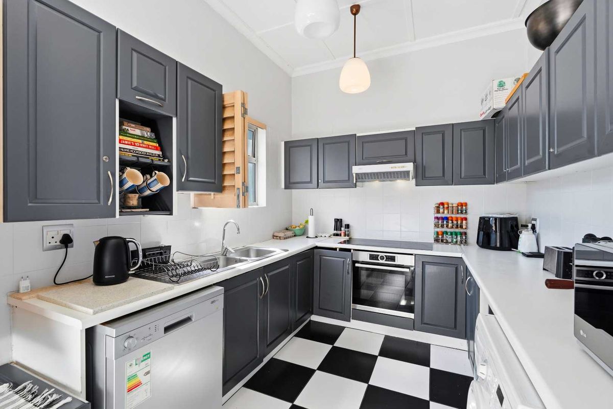 A well-maintained kitchen featuring dark grey cabinetry, white countertops, a built-in oven with hob, and classic checkerboard floor tiling.