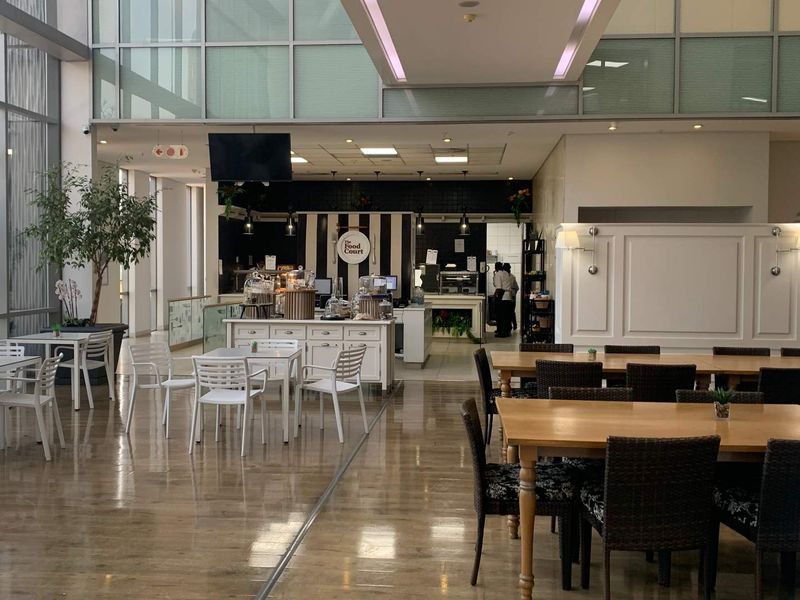 Spacious open-plan office food court area featuring high ceilings, large glass windows for natural light, and a dedicated service counter.