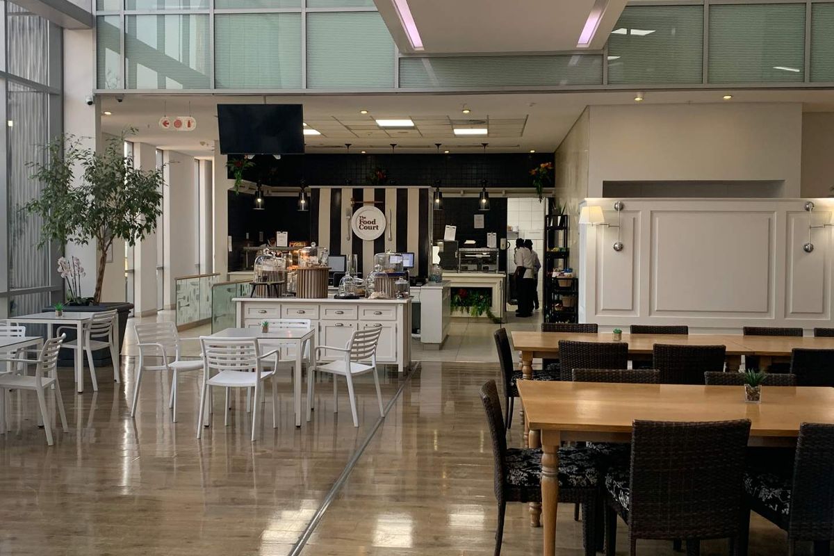 Spacious open-plan office food court area featuring high ceilings, large glass windows for natural light, and a dedicated service counter.