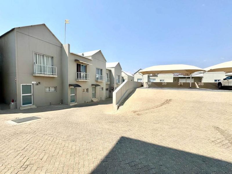 Exterior view of a townhouse complex featuring paved driveway access, covered carport parking, and multi-level units with balcony access.