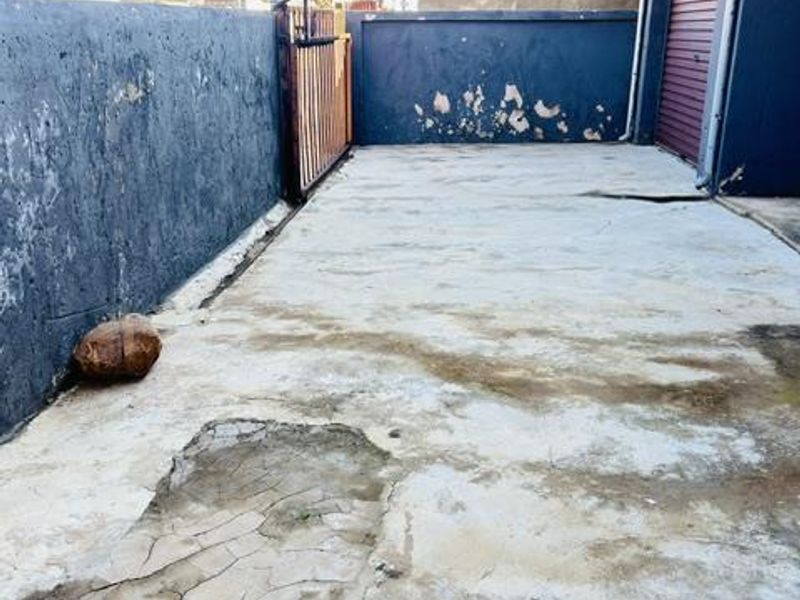 Rear exterior area featuring a concrete paved surface, boundary walls, and a roller shutter door access point.