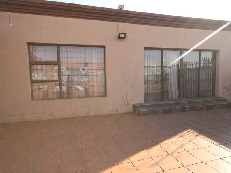 Rear exterior view of the property featuring a tiled patio area, sliding glass doors with security bars, and visible exterior wall plaster cracking.