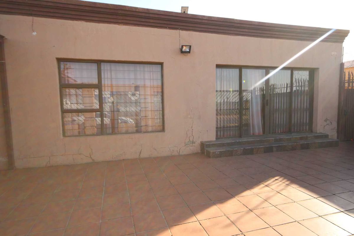 Rear exterior view of the property featuring a tiled patio area, sliding glass doors with security bars, and visible exterior wall plaster cracking.