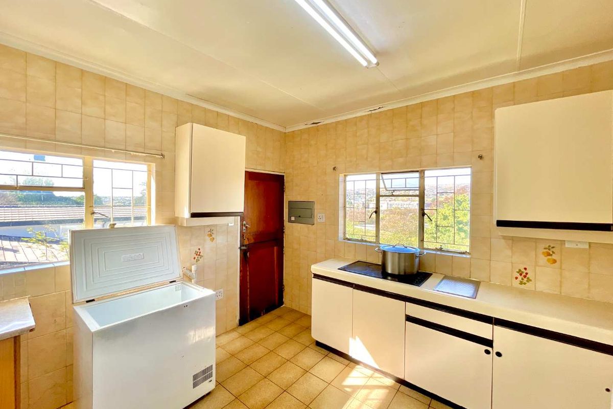 A dated kitchen featuring tiled walls, built-in cabinetry, and large windows providing natural light and neighborhood views.