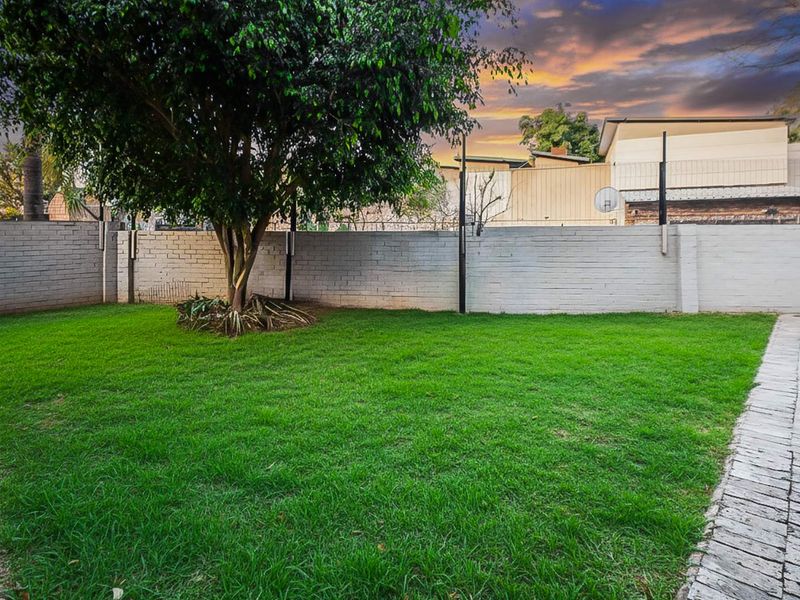 A well-maintained rear garden featuring a lush lawn, paved pathways, and a secure brick boundary wall.