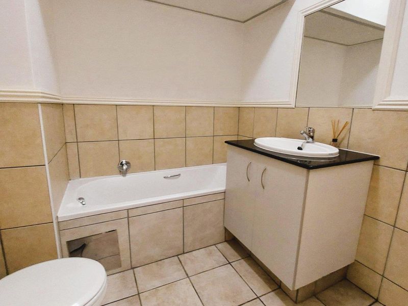 A functional bathroom featuring a built-in bathtub, vanity cabinet with basin, and neutral ceramic tiling throughout.