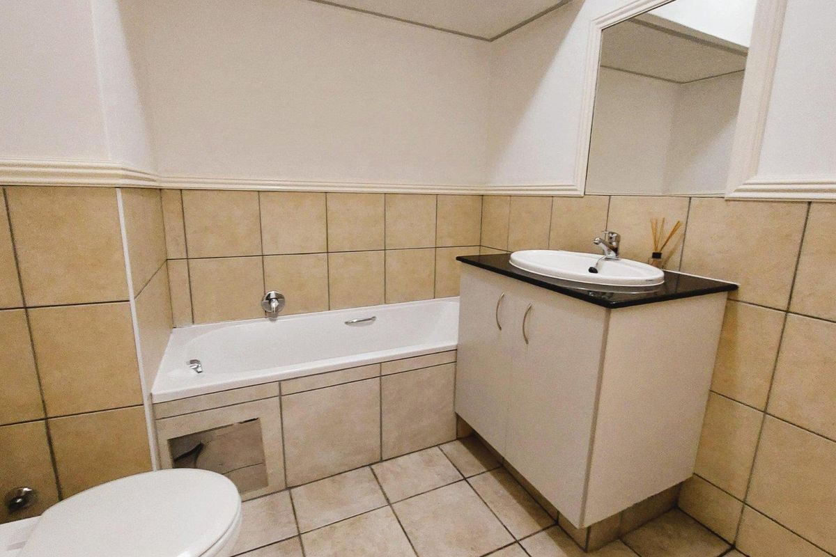 A functional bathroom featuring a built-in bathtub, vanity cabinet with basin, and neutral ceramic tiling throughout.
