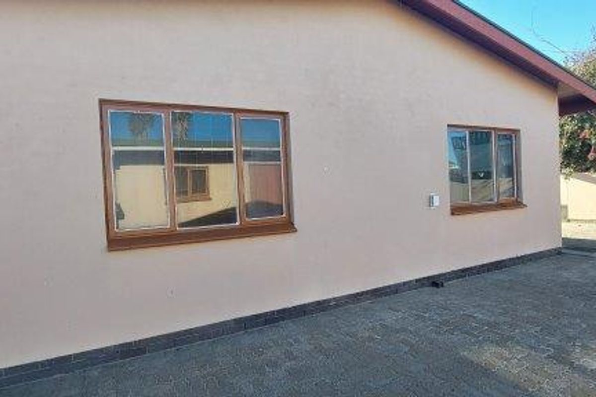 A view of the exterior rear elevation featuring a paved courtyard area, rendered walls, and timber-framed windows.