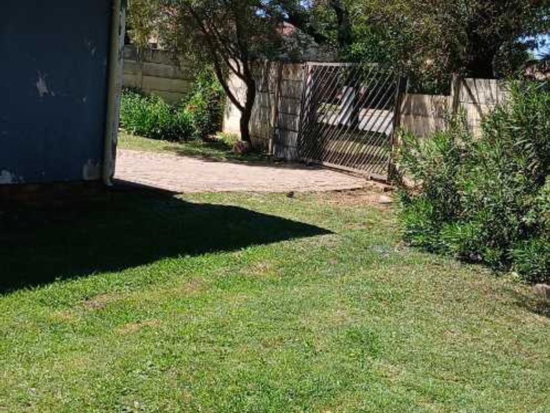 A view of the rear garden area featuring a paved section, boundary wall, and metal gate, with visible wear to the exterior wall paint.