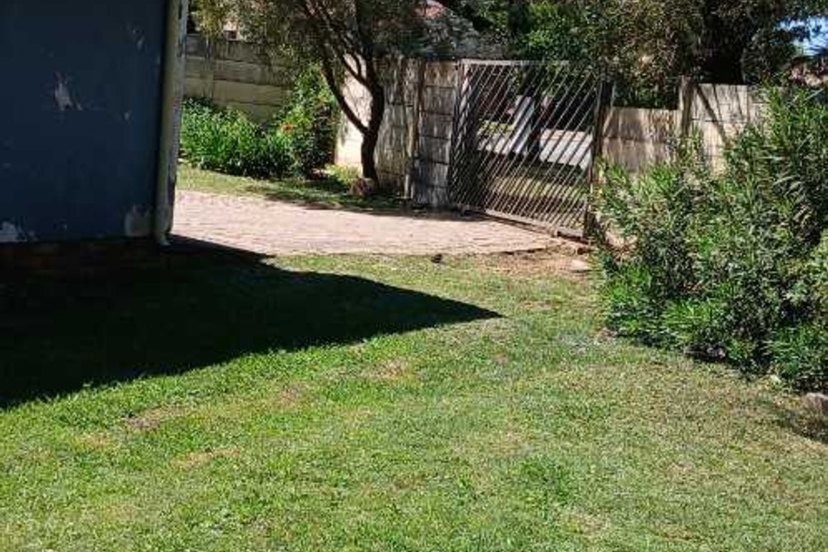 A view of the rear garden area featuring a paved section, boundary wall, and metal gate, with visible wear to the exterior wall paint.