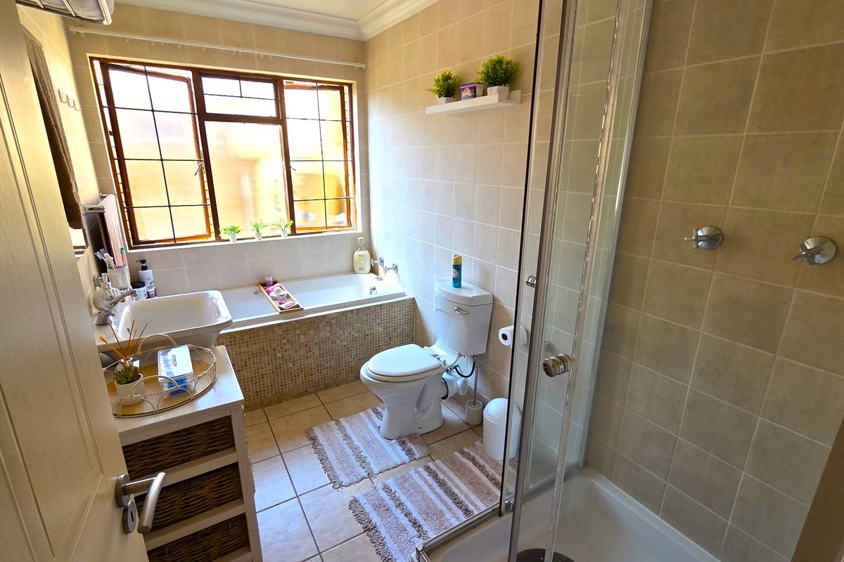 A functional bathroom featuring a built-in bathtub, separate glass-enclosed shower, toilet, and basin with neutral ceramic tiling throughout.