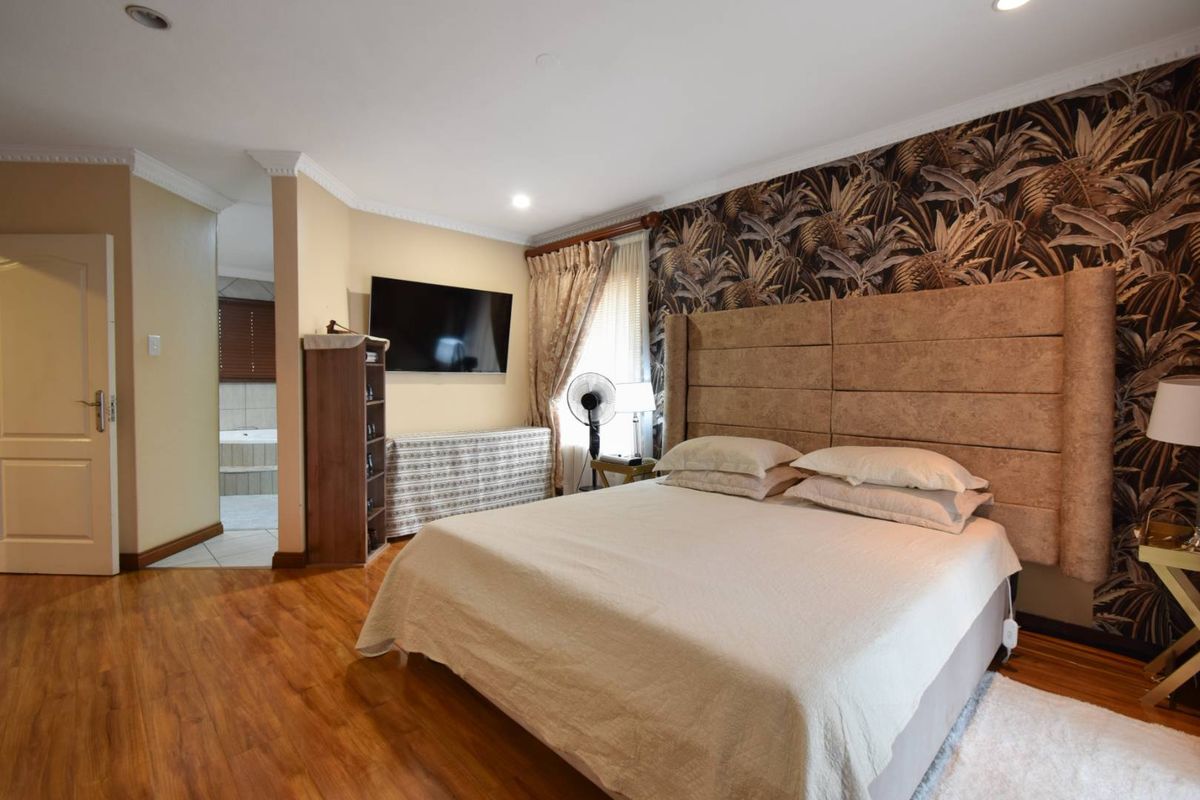 Spacious bedroom featuring wood-look flooring, a decorative feature wall, and an en-suite bathroom access.