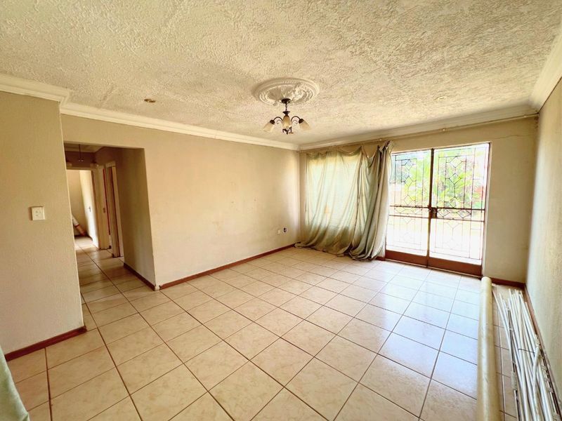 An empty living room featuring tiled flooring, a decorative ceiling rose, and a sliding glass door with a security gate leading to the exterior.