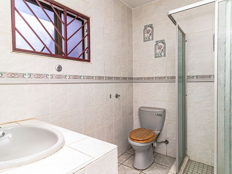 A functional bathroom featuring a shower enclosure, built-in vanity with basin, and toilet, finished with neutral wall tiles and a decorative border.