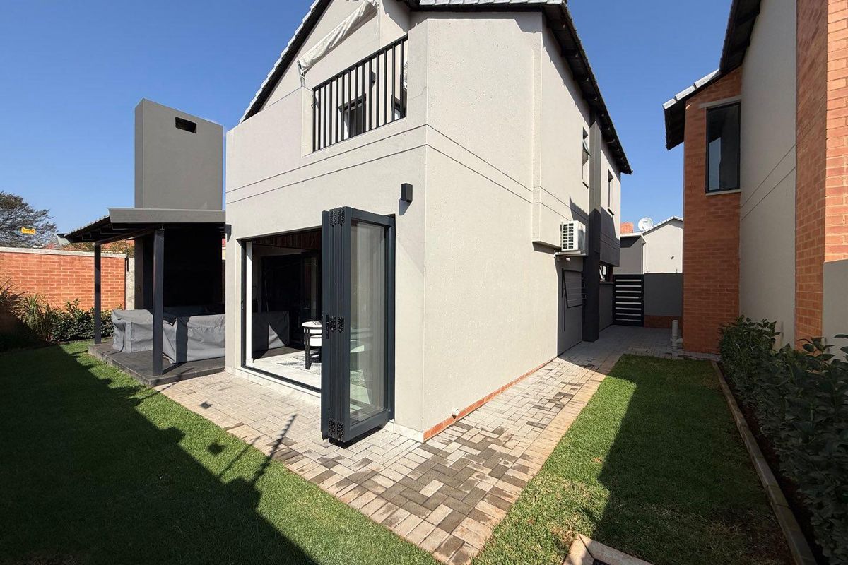 Rear view of the property featuring a paved patio area, manicured lawn, and modern bi-fold doors leading into the living space.