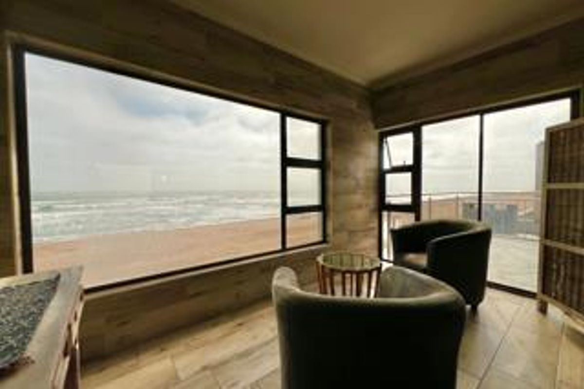 A bright living area featuring expansive floor-to-ceiling windows with direct ocean views and wood-look flooring, providing a seamless connection to the coastal environment.