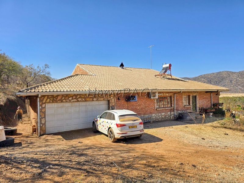 Front exterior view of a brick and stone-clad small holding property featuring a tiled roof, solar water heater, and attached garage.