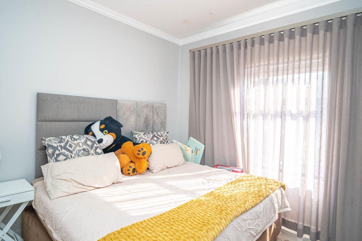 A well-maintained bedroom featuring neutral wall tones, crown molding, and floor-to-ceiling curtains providing natural light.
