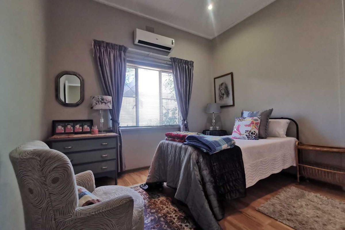A well-maintained bedroom featuring laminate flooring, a wall-mounted air conditioning unit, and a window with fitted blinds.