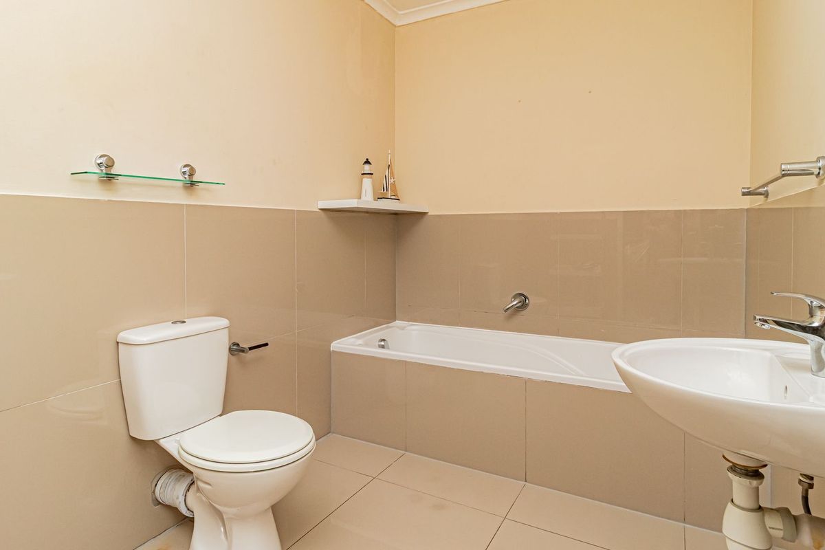 A functional bathroom featuring a bathtub, pedestal basin with chrome mixer tap, and neutral wall and floor tiling.
