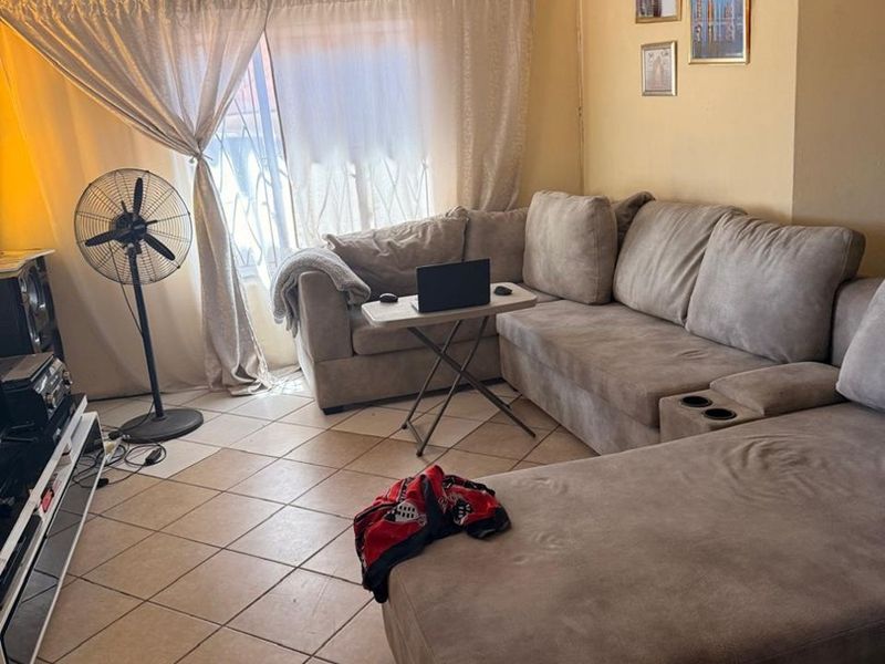 A living room featuring tiled flooring and decorative ceiling tiles, offering a functional space with potential for cosmetic updates.