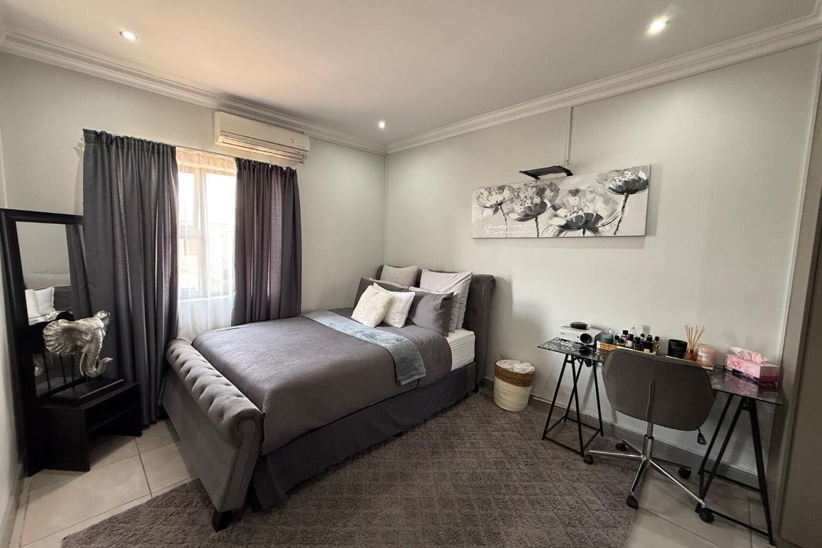 A well-maintained bedroom featuring tiled flooring, recessed downlighting, and a wall-mounted split-system air conditioning unit.