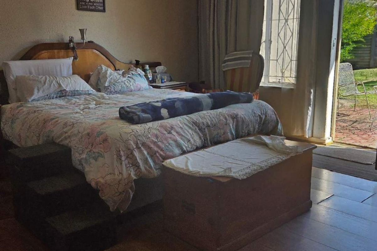 A bedroom featuring timber flooring and direct access to an outdoor patio area through a sliding door with security gate.