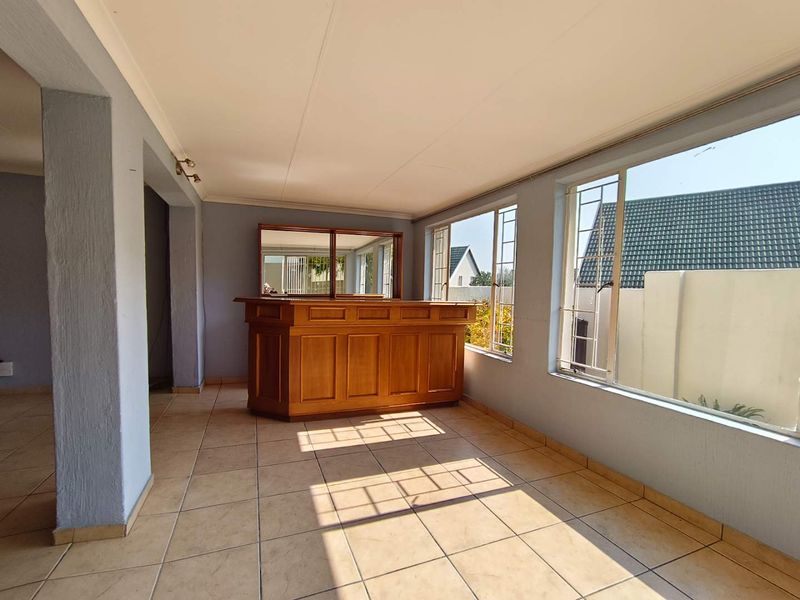 A bright, open-plan bar area featuring a built-in wooden counter, tiled flooring, and large windows providing ample natural light.