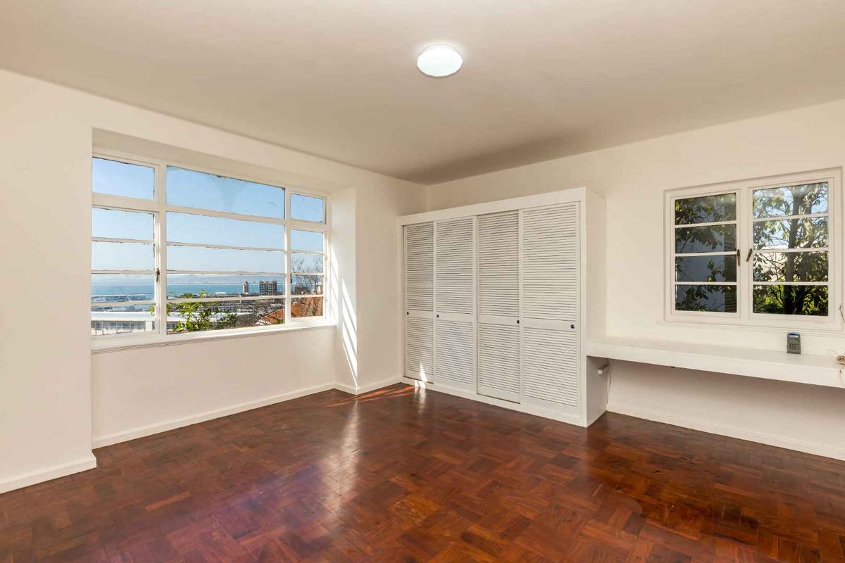 Spacious bedroom featuring classic parquet flooring, built-in cupboards, a fitted desk, and large windows offering expansive coastal views.