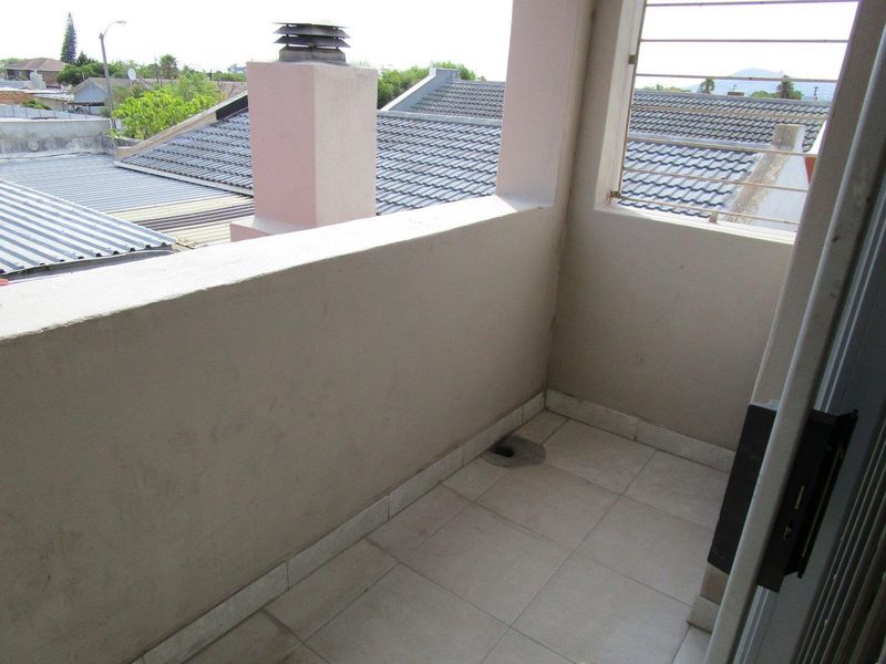 A compact balcony featuring tiled flooring and a solid balustrade wall, offering an elevated view of the surrounding neighborhood rooftops.
