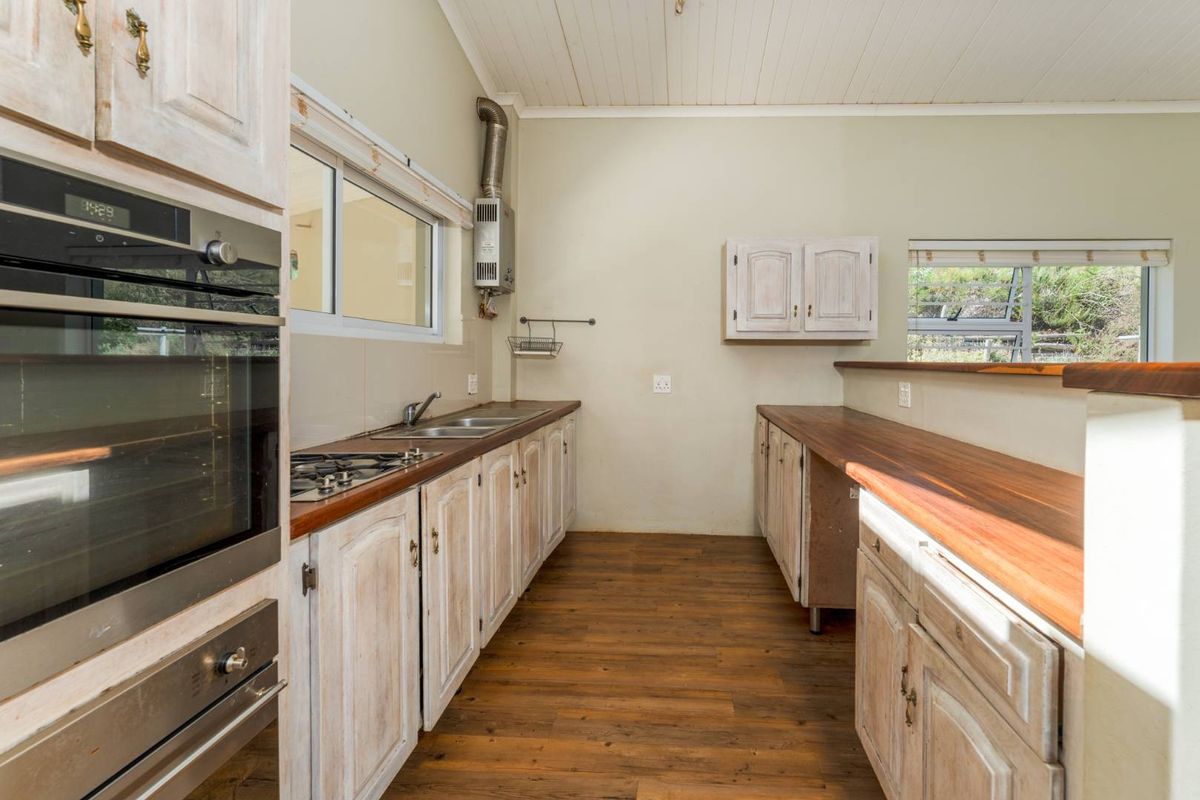 A functional kitchen featuring wooden countertops, built-in oven, gas hob, and ample cabinetry, with a pass-through window overlooking the surrounding landscape.