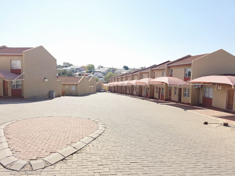 Exterior view of an apartment complex featuring a paved driveway and a row of units with individual carport structures.