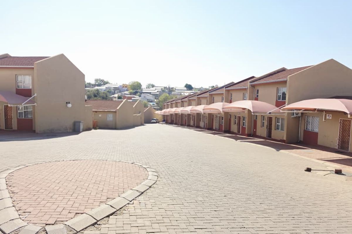 Exterior view of an apartment complex featuring a paved driveway and a row of units with individual carport structures.