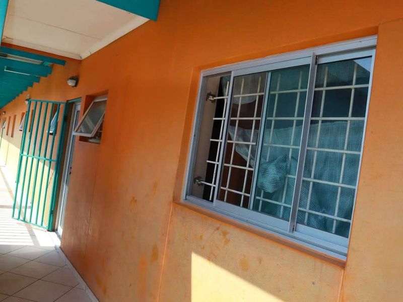 An exterior apartment hallway featuring tiled flooring, a security gate, and a sliding window with security bars.