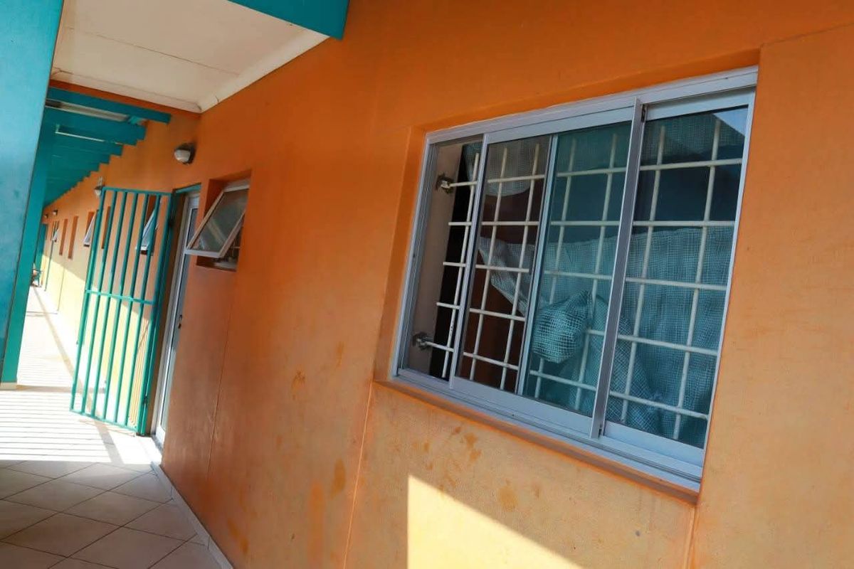 An exterior apartment hallway featuring tiled flooring, a security gate, and a sliding window with security bars.