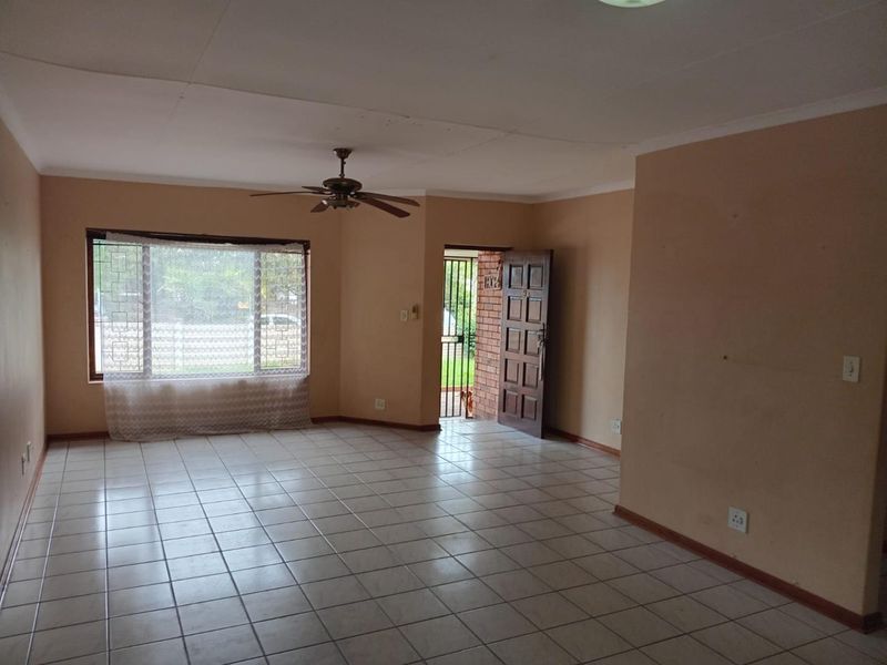 An empty living room featuring tiled flooring, a ceiling fan, and a timber entrance door with an external security gate.