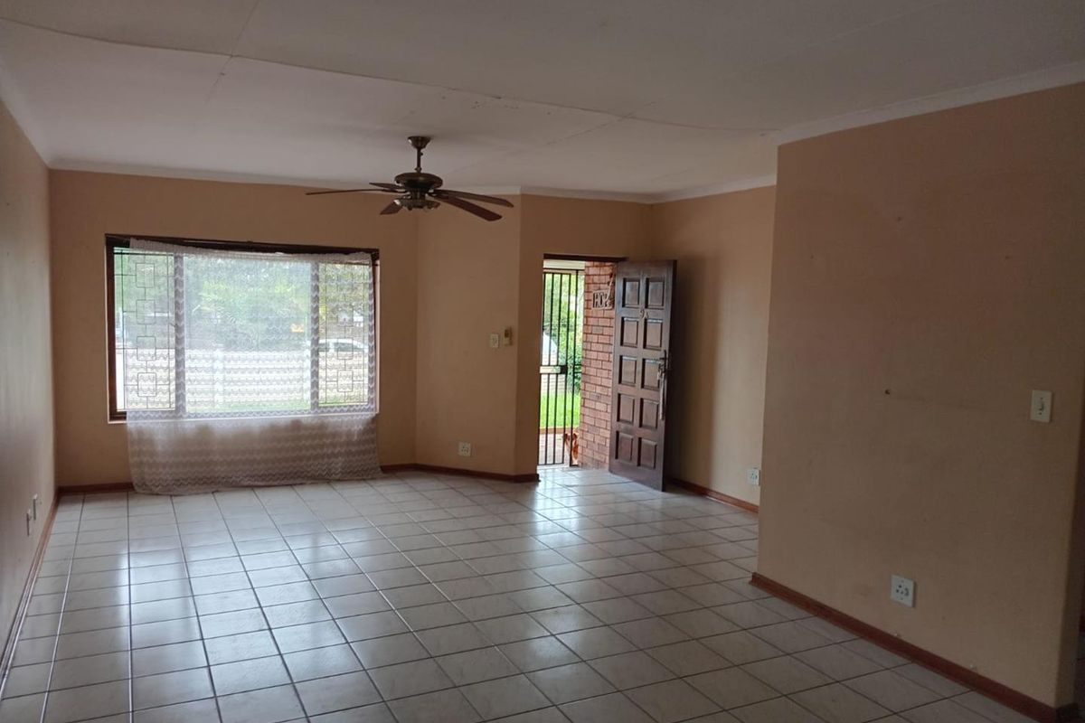 An empty living room featuring tiled flooring, a ceiling fan, and a timber entrance door with an external security gate.